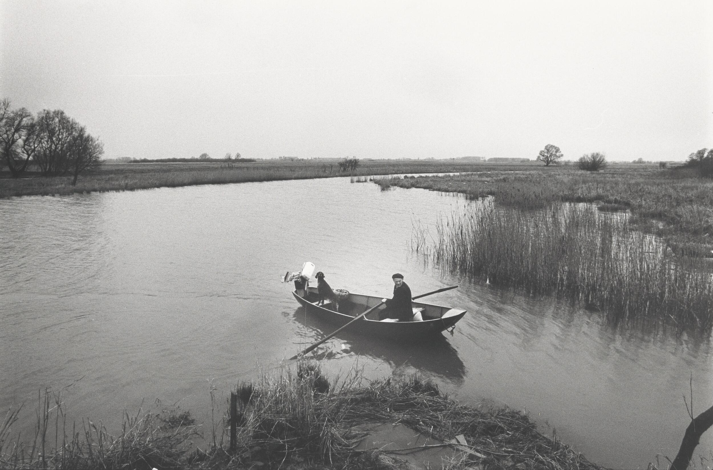 De foto toont Boer Fré Vos met zijn hond in een roeiboot in een van de Biesboschkreken